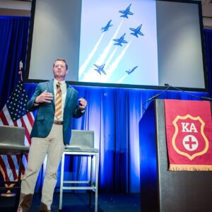 Frank Weisser presenting with jets flying in formation on screen