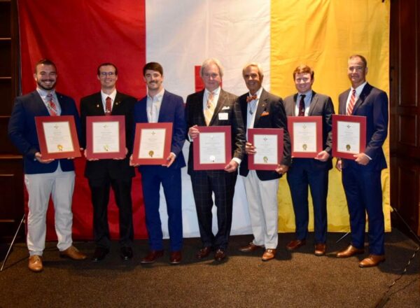 Inductees with certificates in front of large KA flag