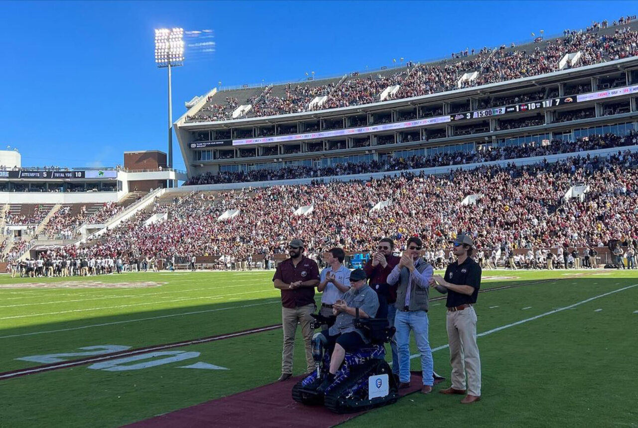 Mississippi State KA brothers on football field with Army Sergeant Jeff Hemenger with stadium full of fans