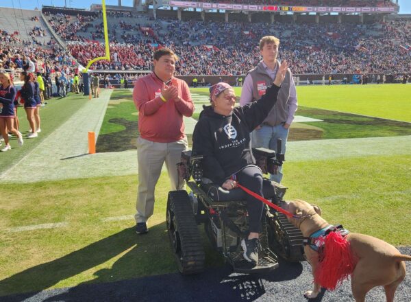 Brooks standing, Hutchinson in track chair, Marks, and dog pork chop on the football field