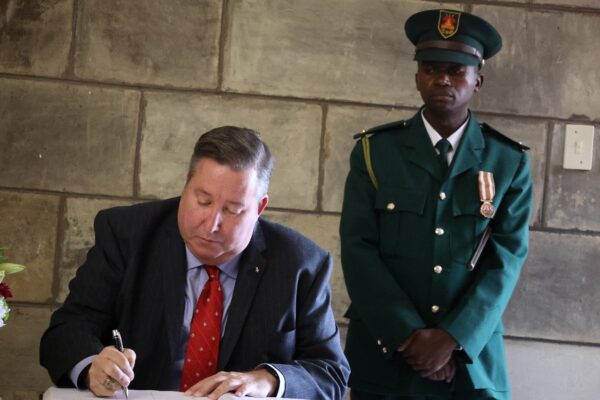 man in suit and tie seated and signing paper with man in uniform standing