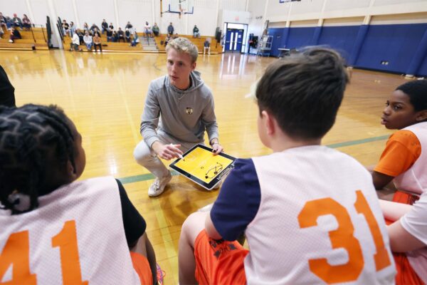 coach kneeling on basketball court in front of sitting team