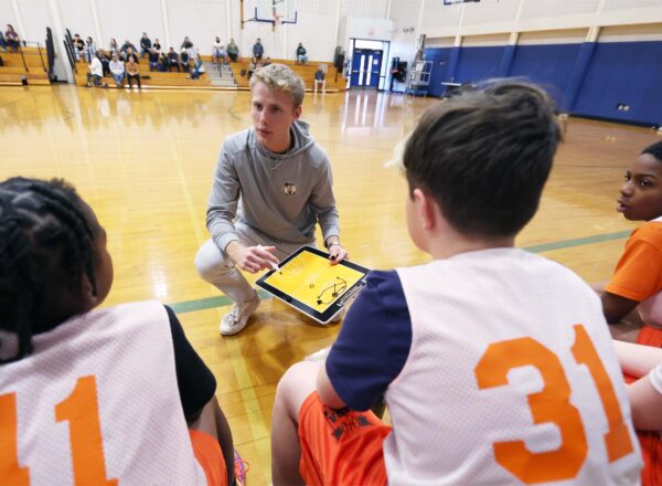coach kneeling on basketball court in front of sitting team