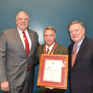 three men in suits with center holding award