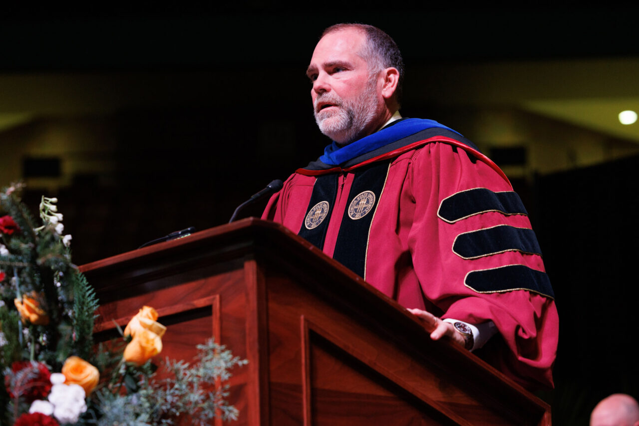 man in graduation attire speaking from podium
