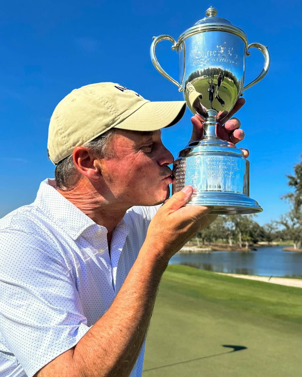 man in golf hat and polo kissing golf trophy