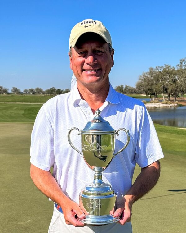 man in golf hat and polo holding golf trophy