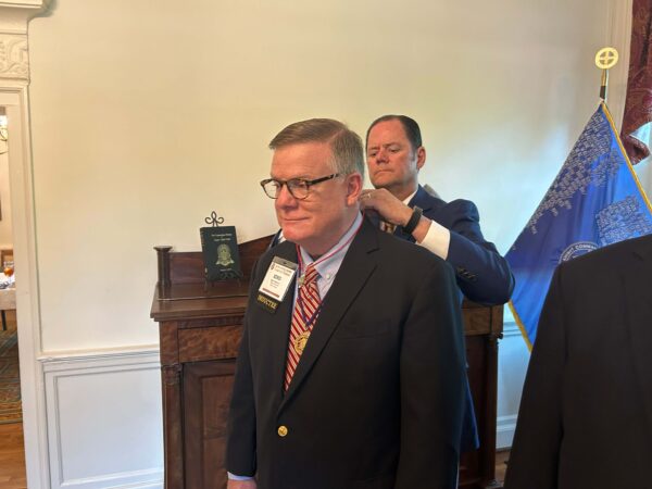 man in suit putting jewel on cord around neck of another man in suit