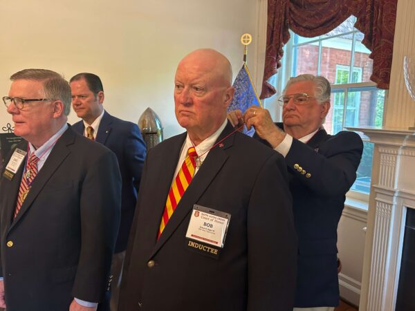 man in suit putting jewel on cord around neck of another man in suit