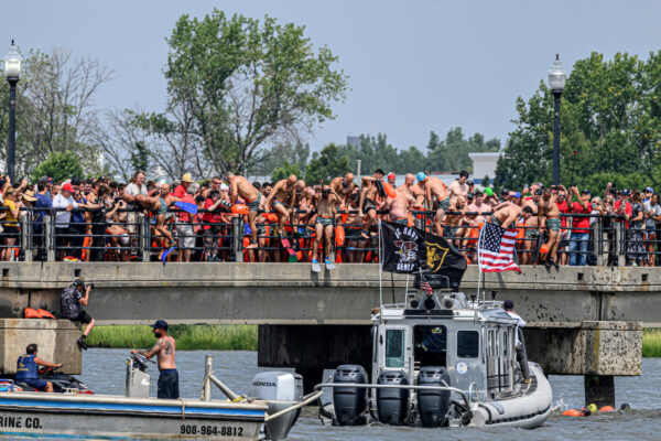men jumping off bridge into river for swim