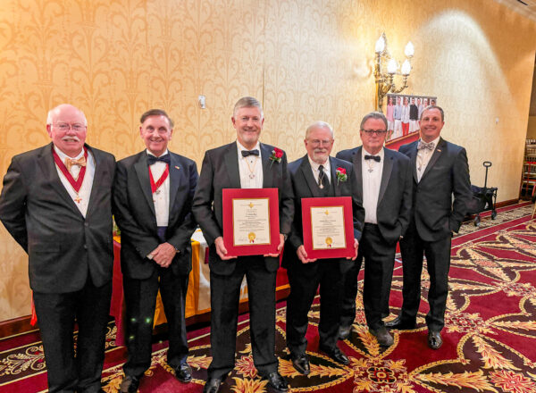 men in tuxes, two in the middle holding certificates