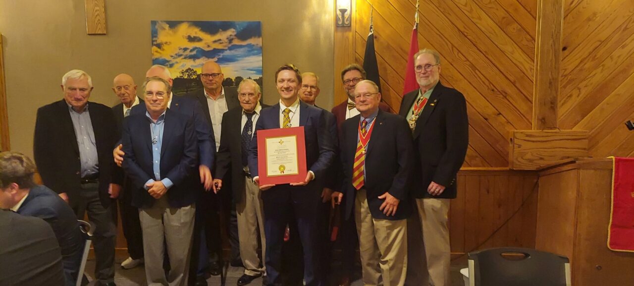 group of men in jackets, one in center holding certificate