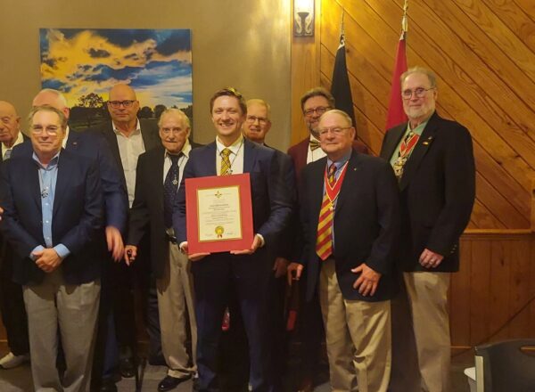 group of men in jackets, one in center holding certificate